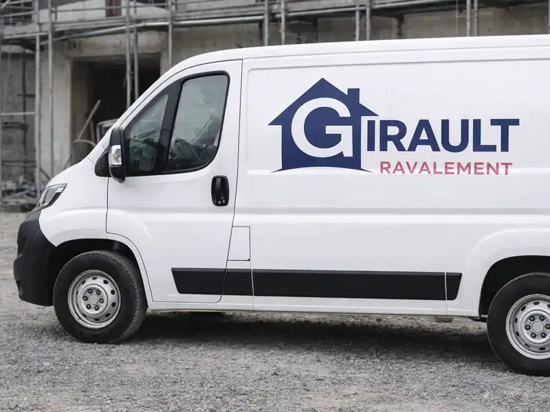 Une camionnette blanche portant le logo de Girault Ravalement et l'ic&ocirc;ne d'une maison stylis&eacute;e est gar&eacute;e sur du gravier devant un b&acirc;timent en construction, avec des &eacute;chafaudages.